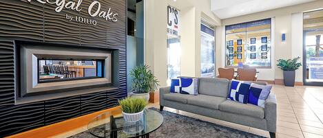 A lobby with a seating area featuring a sofa and a glass table, a potted plant, and a wall-mounted display.