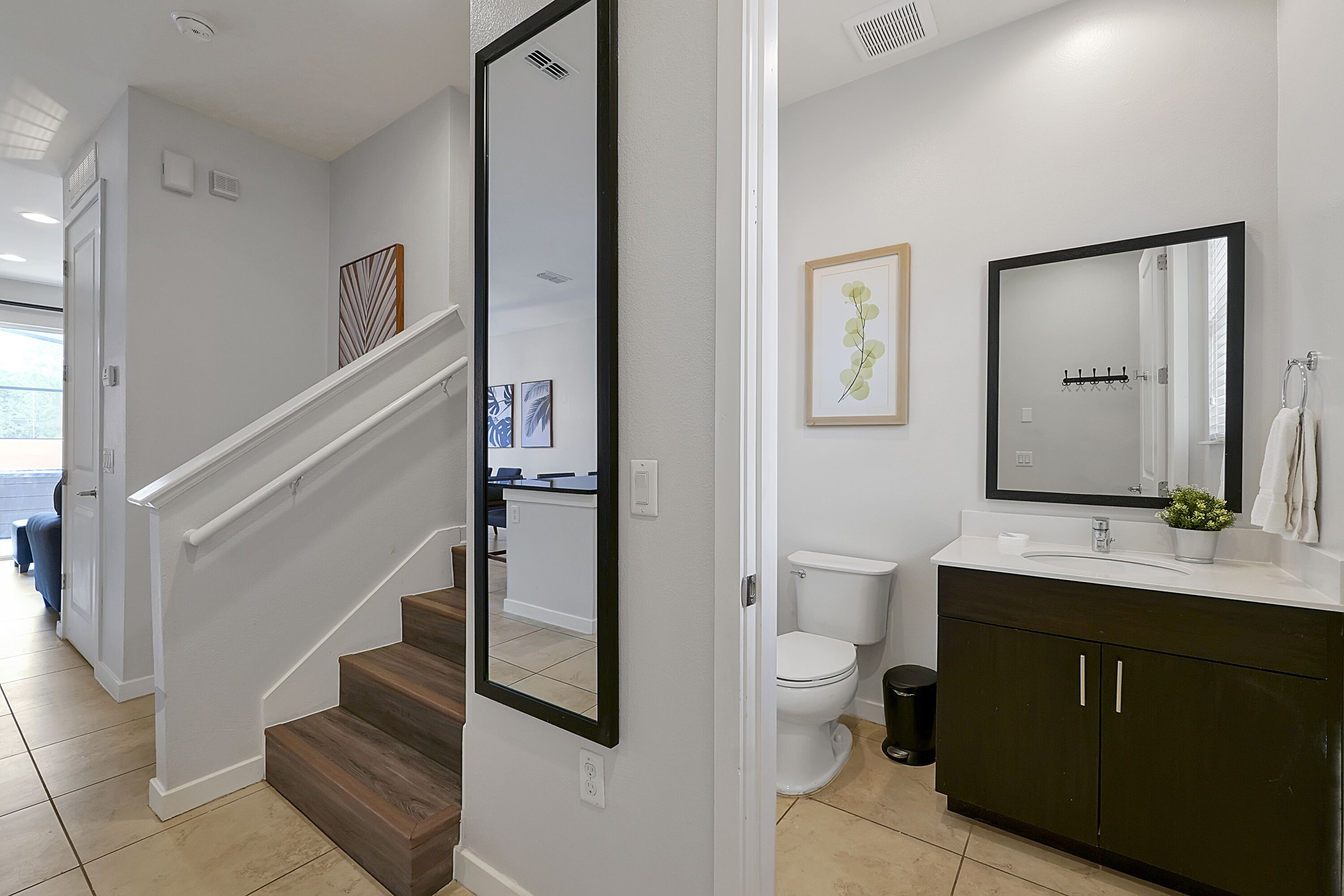 A modern bathroom with a white toilet, dark cabinets, and a large mirror.