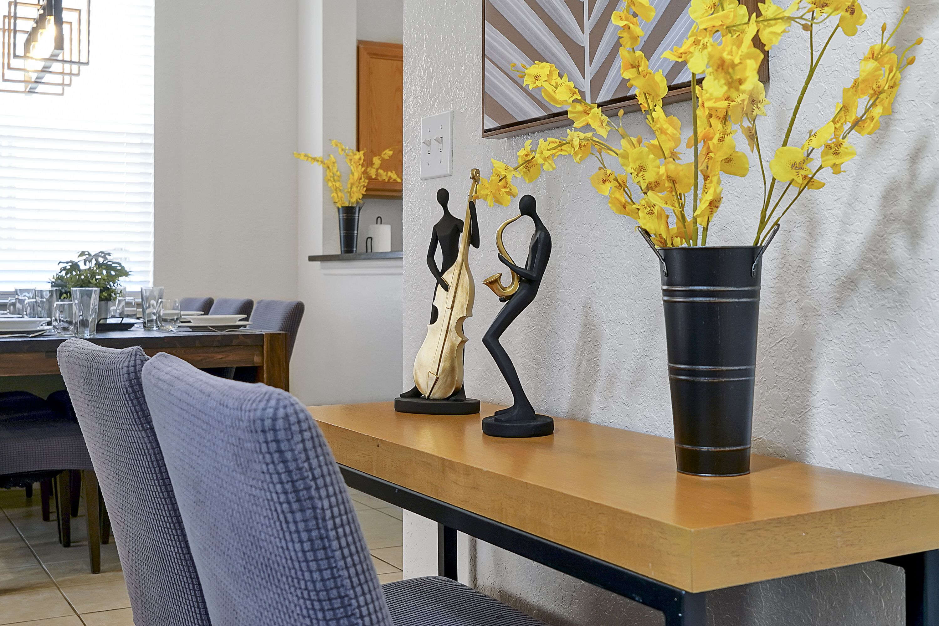 A dining area with a wooden table, chairs, and a vase with yellow flowers.