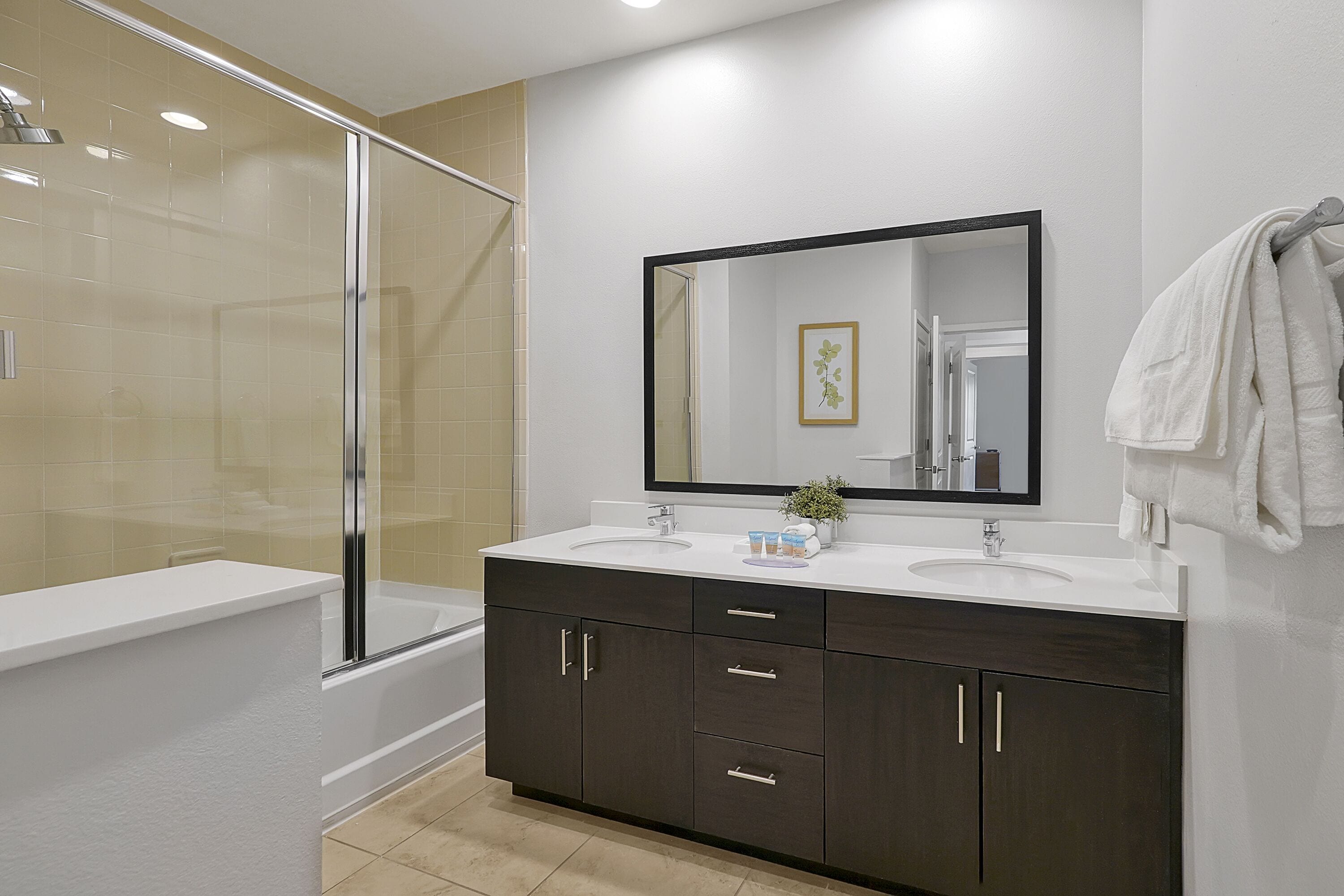 A modern bathroom with a glass shower enclosure, a white sink, dark cabinets, and a large mirror.