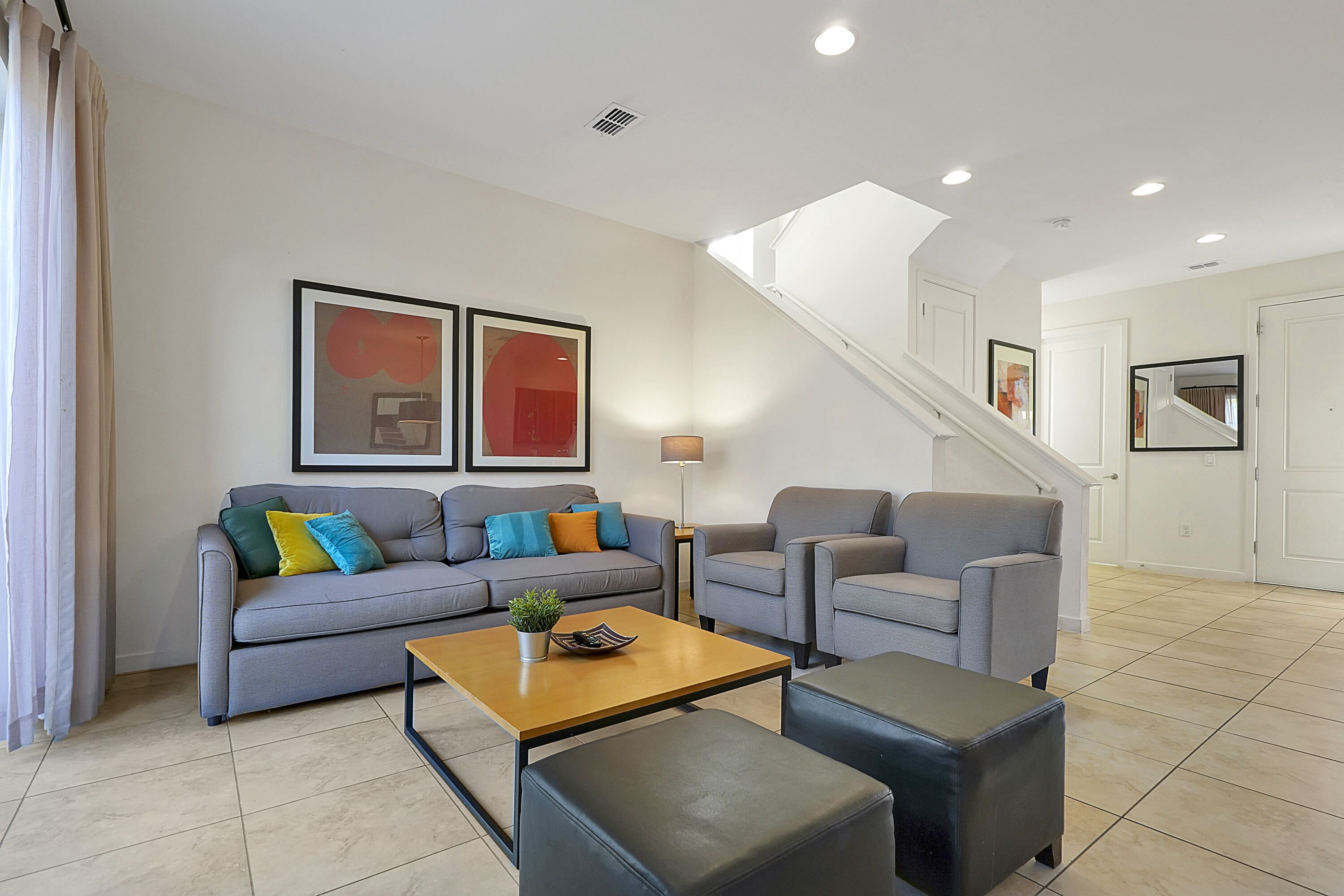 A modern living room with a sofa, armchairs, a coffee table, and a staircase leading to another room.