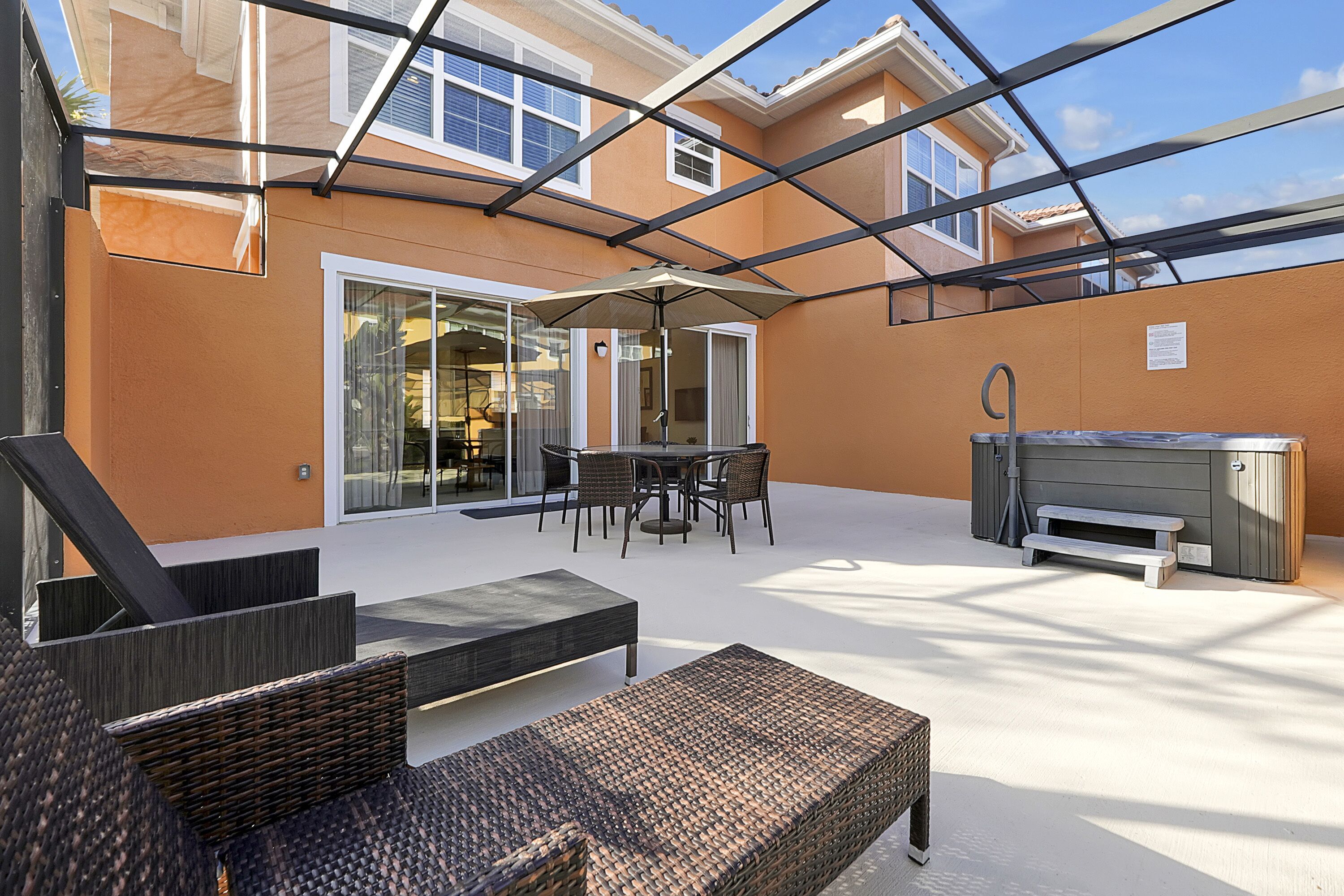 Une terrasse extérieure aménagée avec des meubles en osier, un jacuzzi et une porte vitrée donnant sur un espace intérieur.
