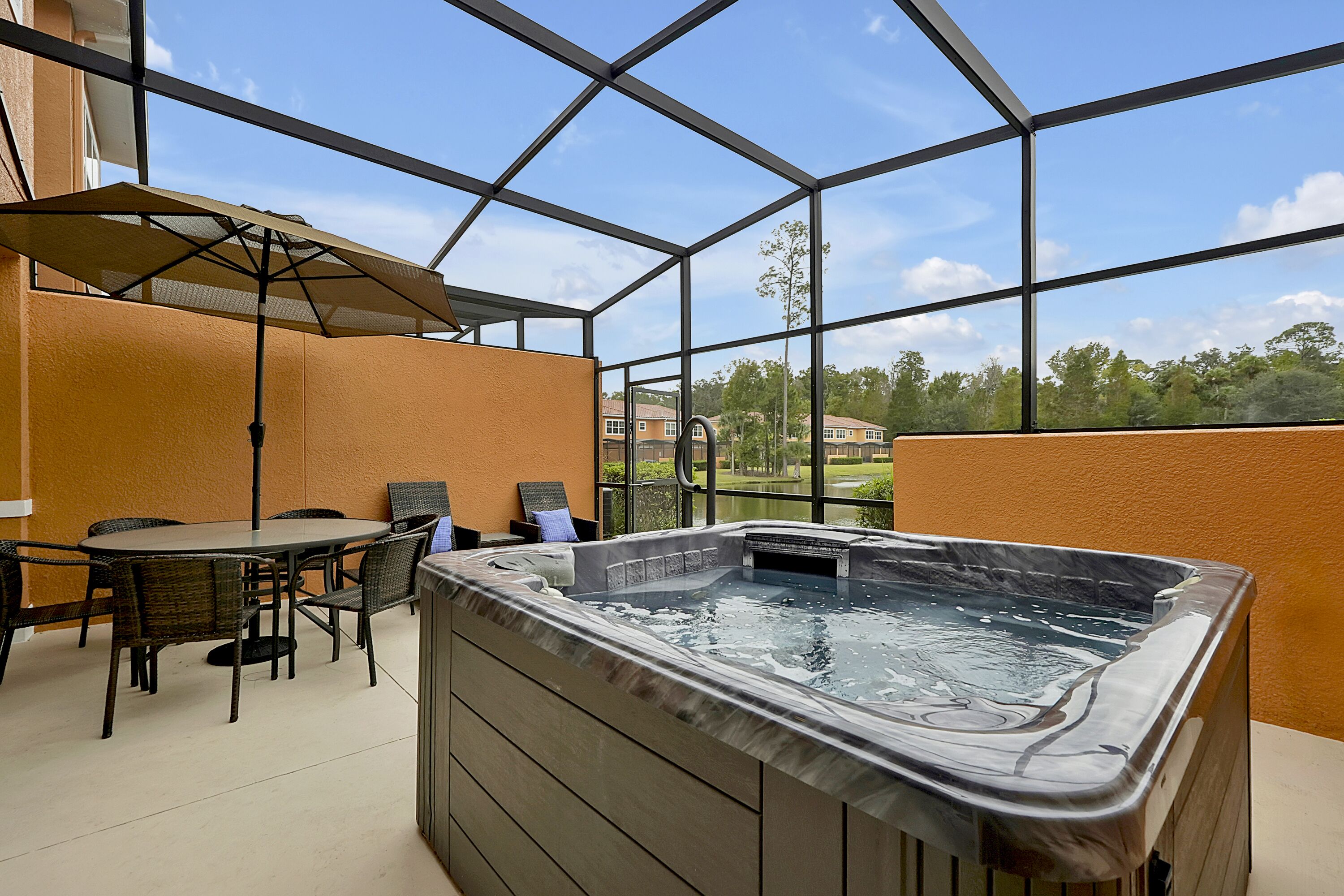 Un jacuzzi installé dans un espace patio fermé par des parois de verre, avec une table et des chaises, donnant sur un quartier résidentiel.