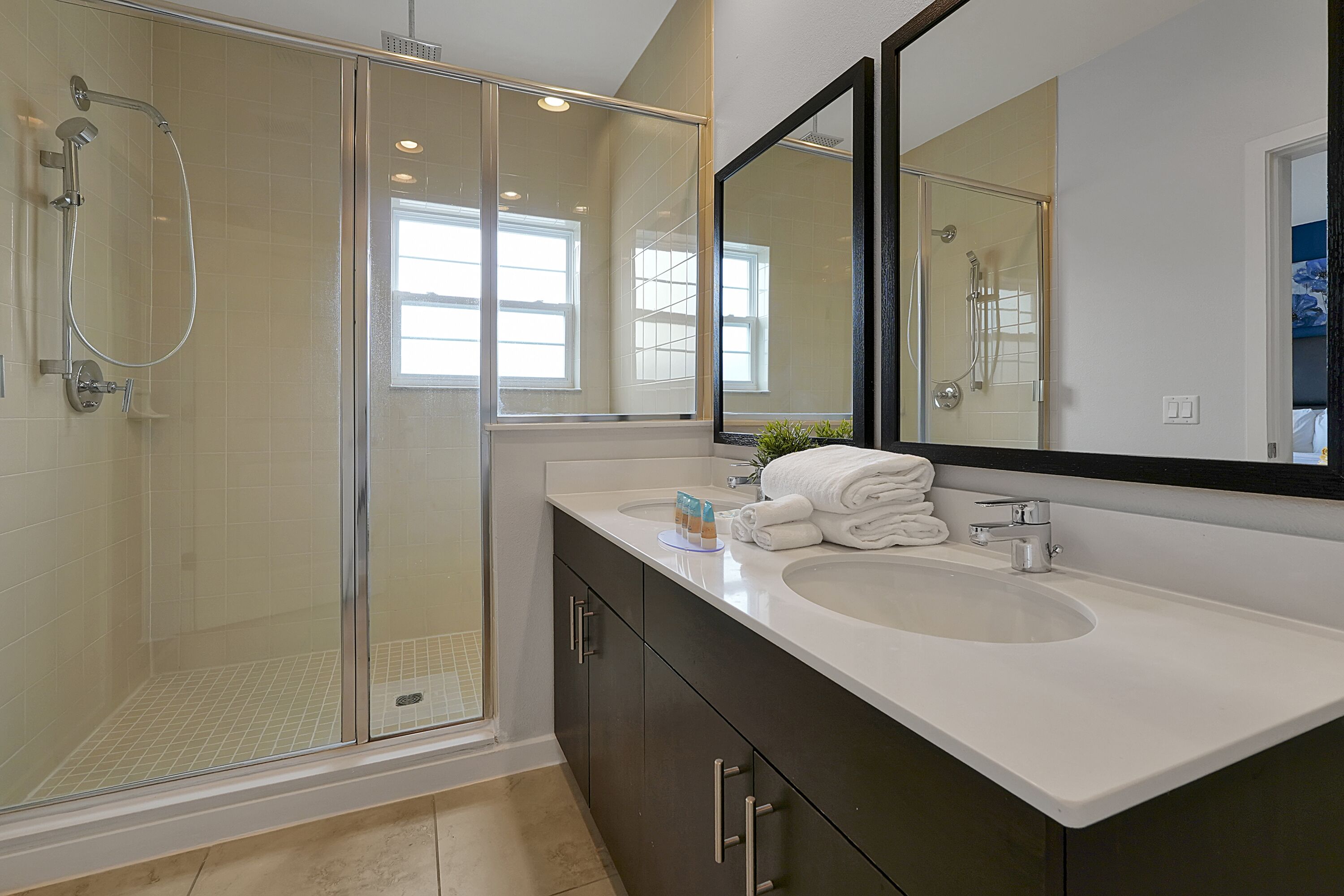 Un baño moderno con ducha de vidrio, un espejo grande y un lavabo blanco.