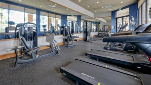 A gym with various exercise equipment, including treadmills, weight machines, and a mirrored wall.