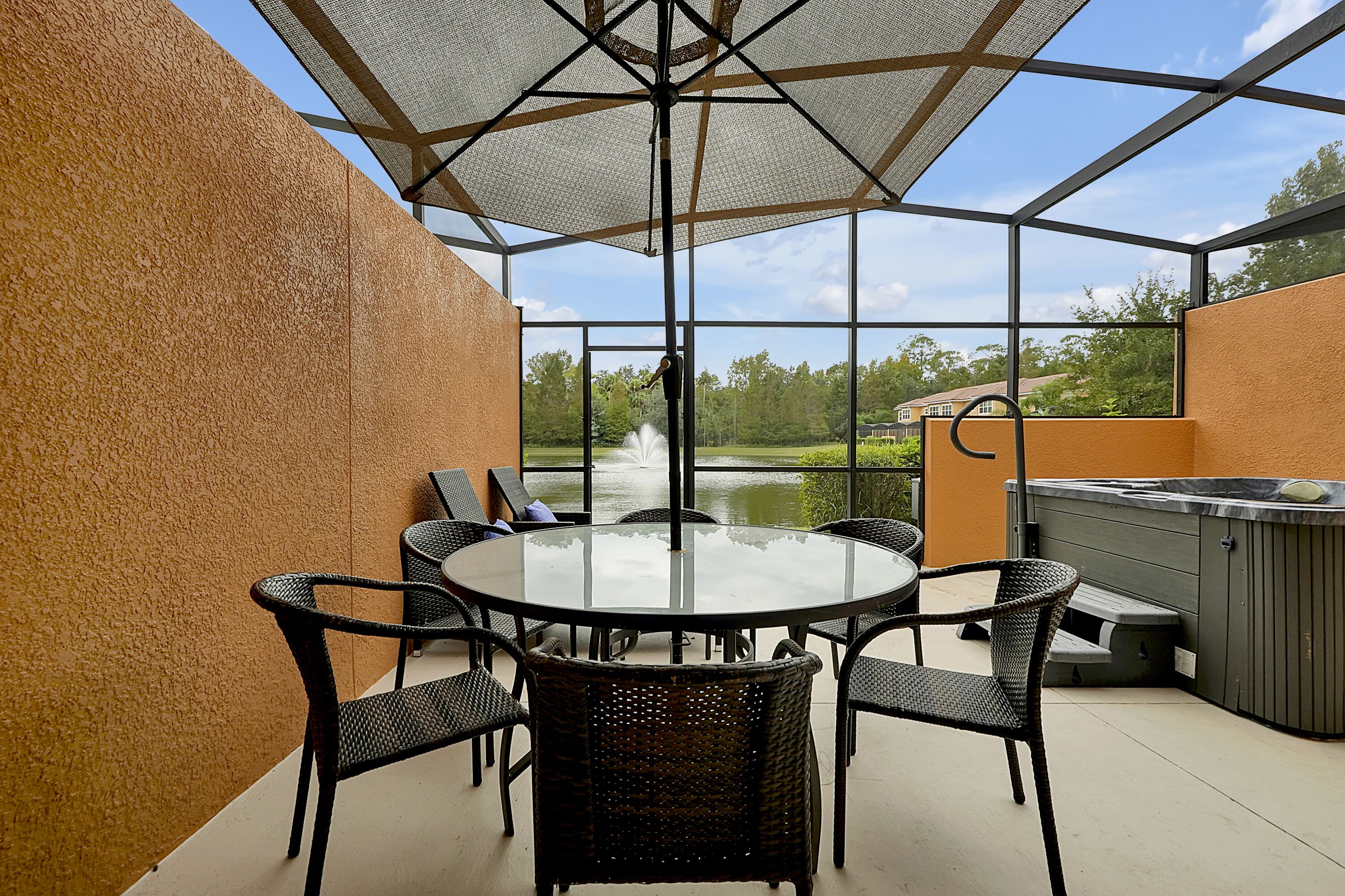 Un patio exterior con una mesa redonda y sillas, un jacuzzi y vistas a un estanque y árboles.