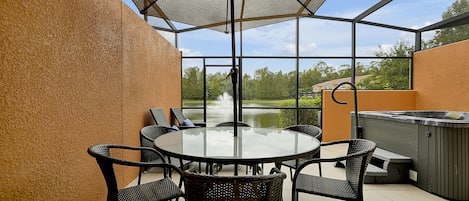 Un patio exterior con una mesa redonda y sillas, un jacuzzi y vistas a un estanque y árboles.