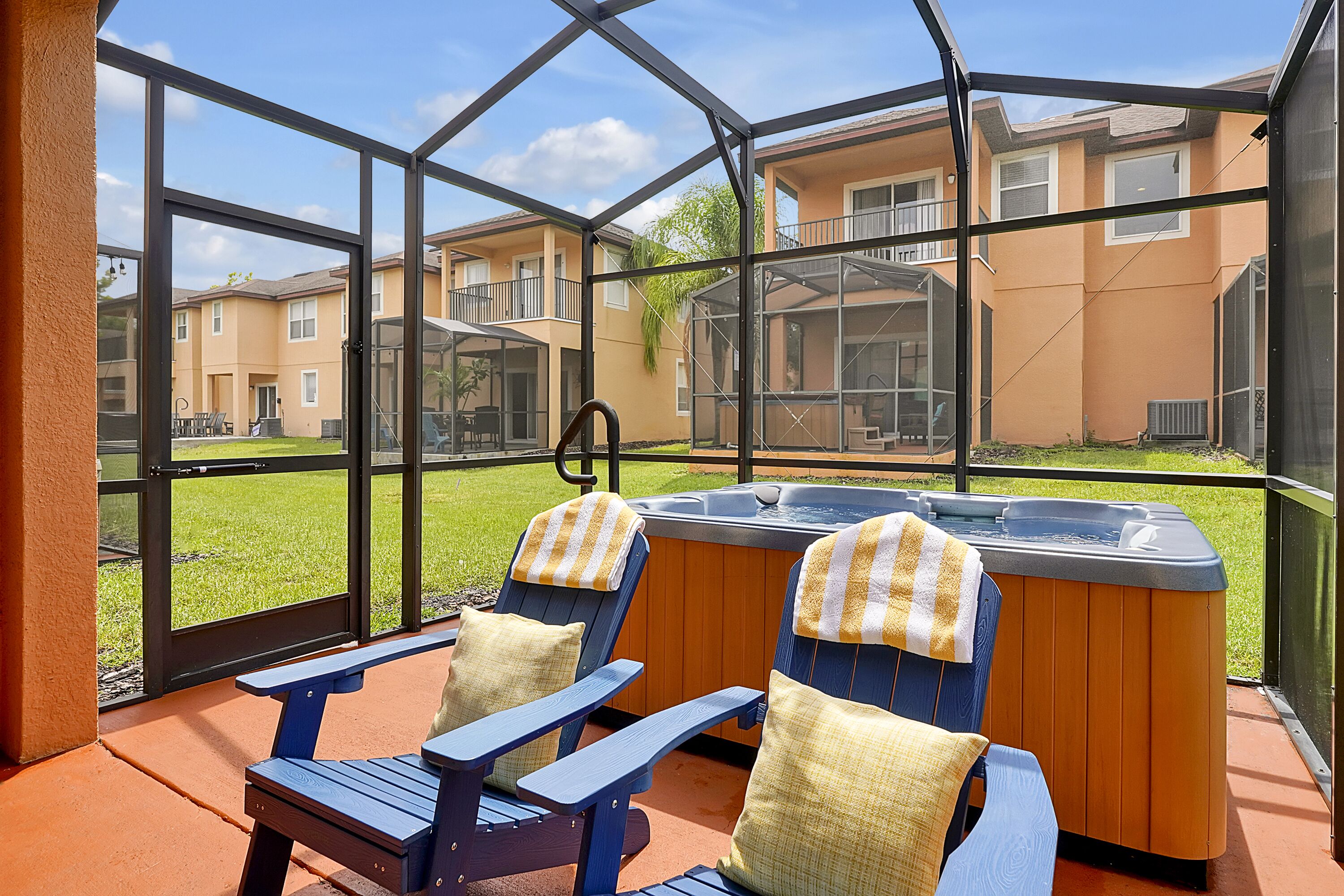 A covered patio with two Adirondack chairs, a hot tub, and a view of apartment buildings.