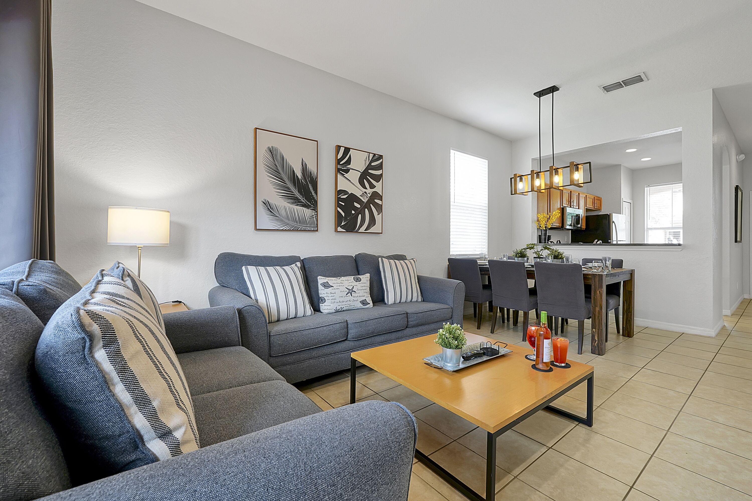 Un salon moderne avec un canapé gris, une table basse en bois et un coin repas, la cuisine étant visible au fond.
