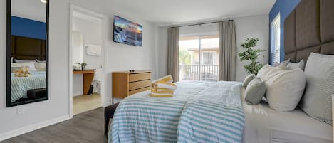 A hotel room with a large bed, a bedside table, a mirror, a window with curtains, and a view of the outside balcony.