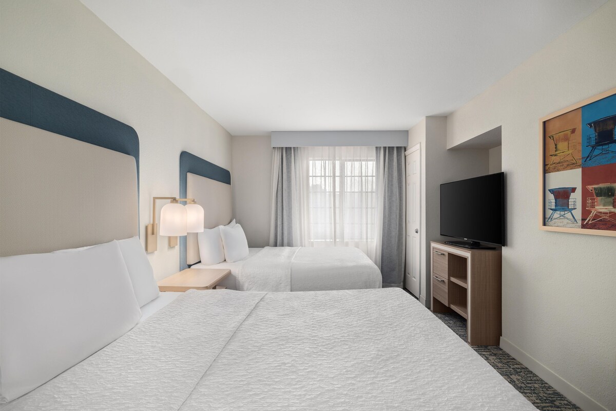 A hotel room with two beds, a TV, and a painting on the wall.