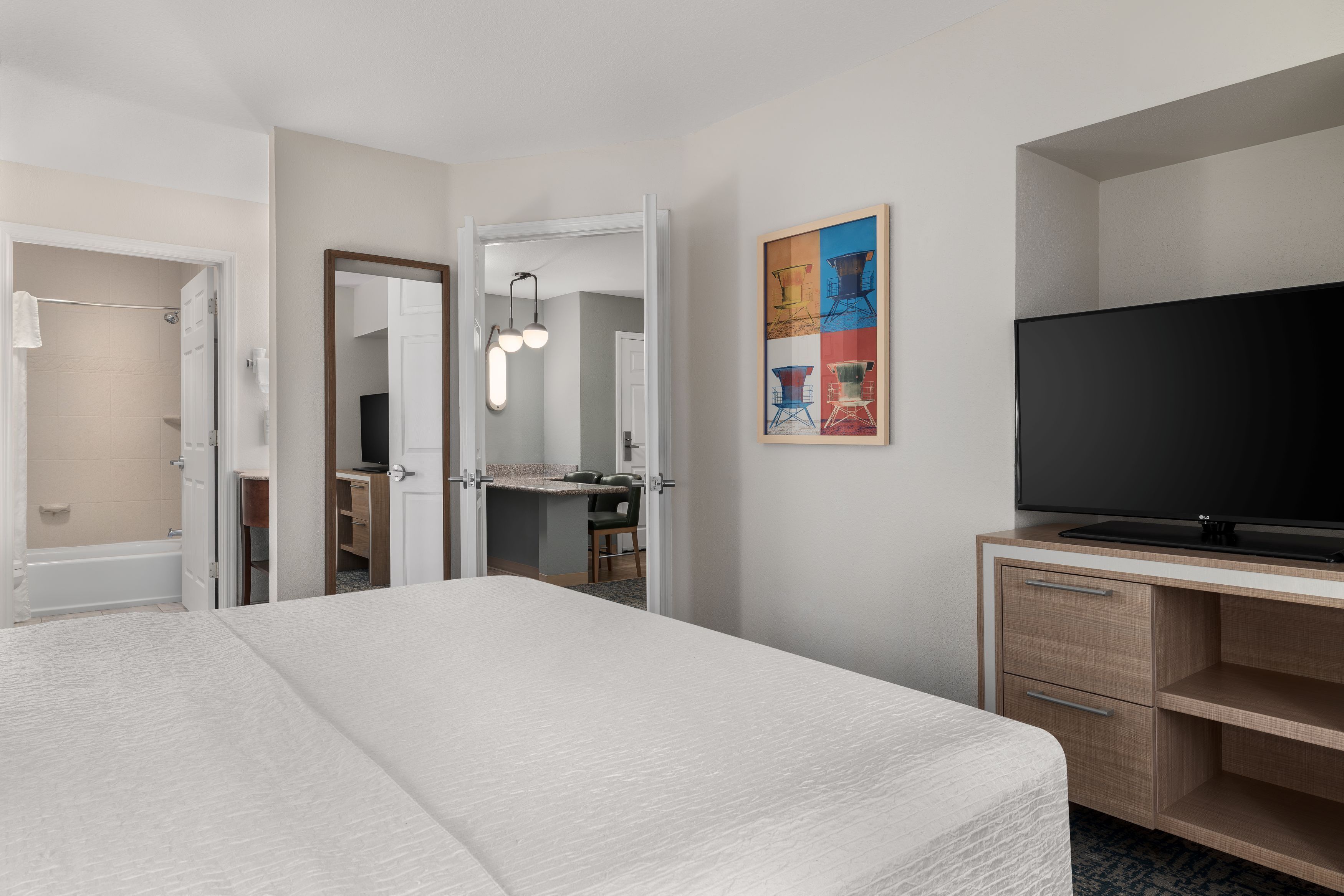 Une chambre d’hôtel comprenant un lit, une t élévision, un bureau avec des tiroirs, une salle de bain avec douche et un miroir.