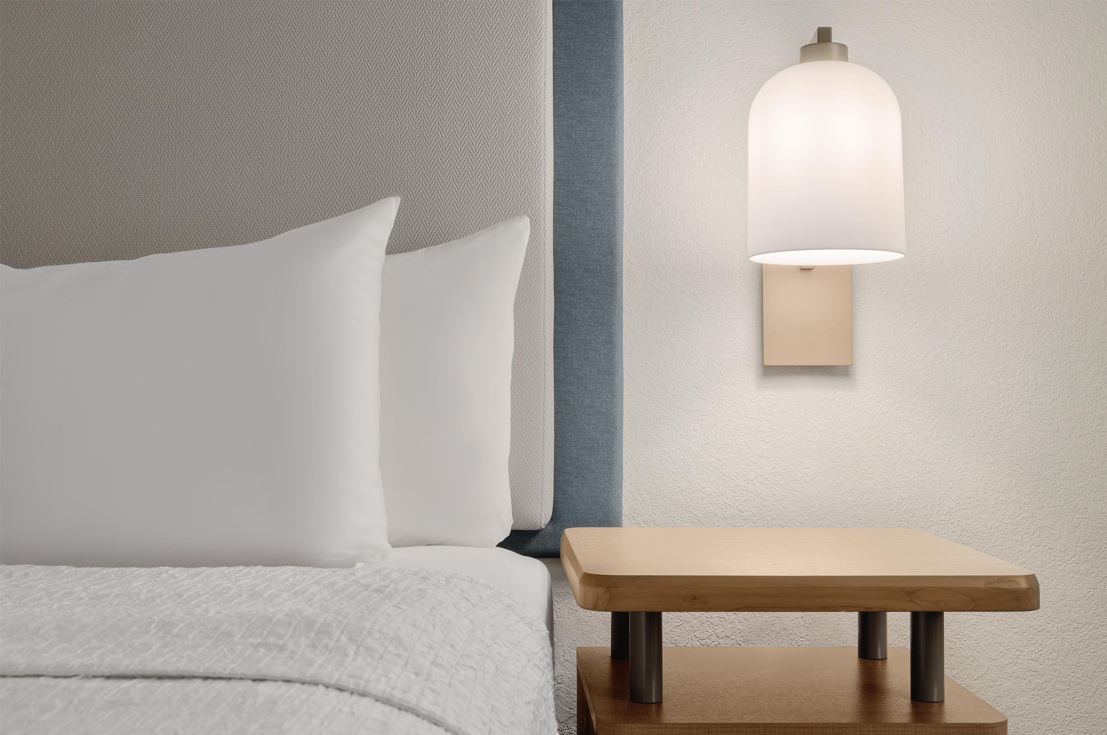 Ein Bett mit weißer Bettwäsche, ein Nachttisch mit einer Lampe und eine strukturierte Wand.