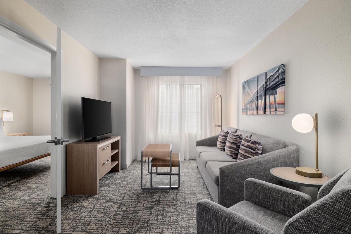 A hotel room with a bed, a TV, a sofa, a coffee table, and a painting on the wall.