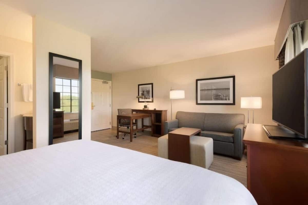 Quarto de hotel com uma cama grande, uma escrivaninha, um sofá, uma TV e quadros nas paredes.