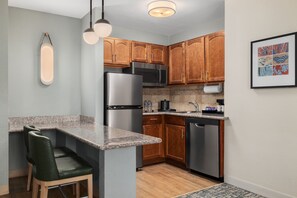 A modern kitchen with granite countertops, stainless steel appliances, wooden cabinets, and a dining area with green chairs. - Homewood Suites by Hilton Jacksonville Deerwood Park (Jacksonville)