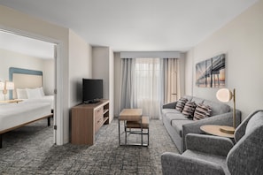 A hotel room with a bed, a TV, a sofa, a small table, and a painting on the wall.