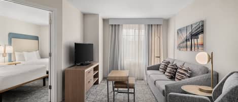 A hotel room with a bed, a TV, a sofa, a small table, and a painting on the wall.