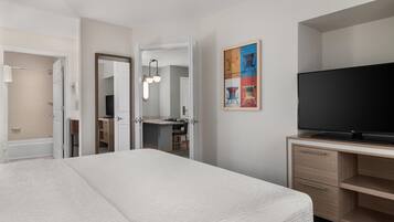 A hotel room with a bed, a TV, a desk, and a bathroom visible through an open door.