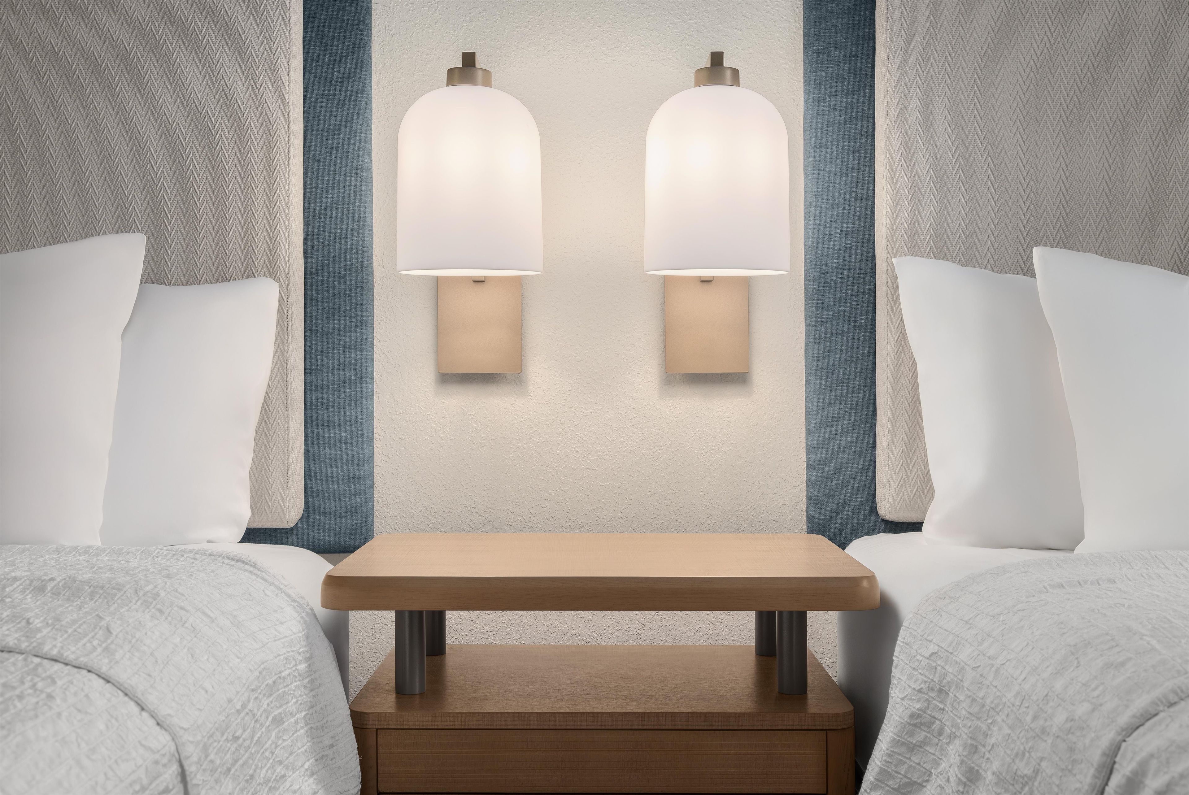 A hotel room with two beds, a wooden nightstand, and wall-mounted lamps.