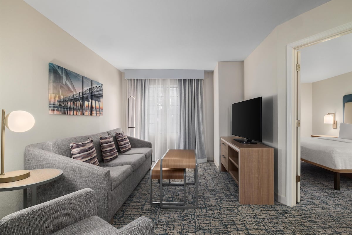 Quarto de hotel com sofá, mesa de madeira, televisão e cama.