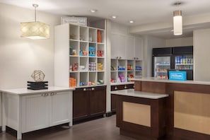 A hotel reception area with a white counter, a minibar, and a sign welcoming guests. - Homewood Suites by Hilton Jacksonville Deerwood Park (Jacksonville)