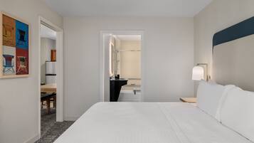 Une chambre d’hôtel avec un grand lit, une table de chevet, un bureau et une salle de bain visible à travers une porte ouverte.