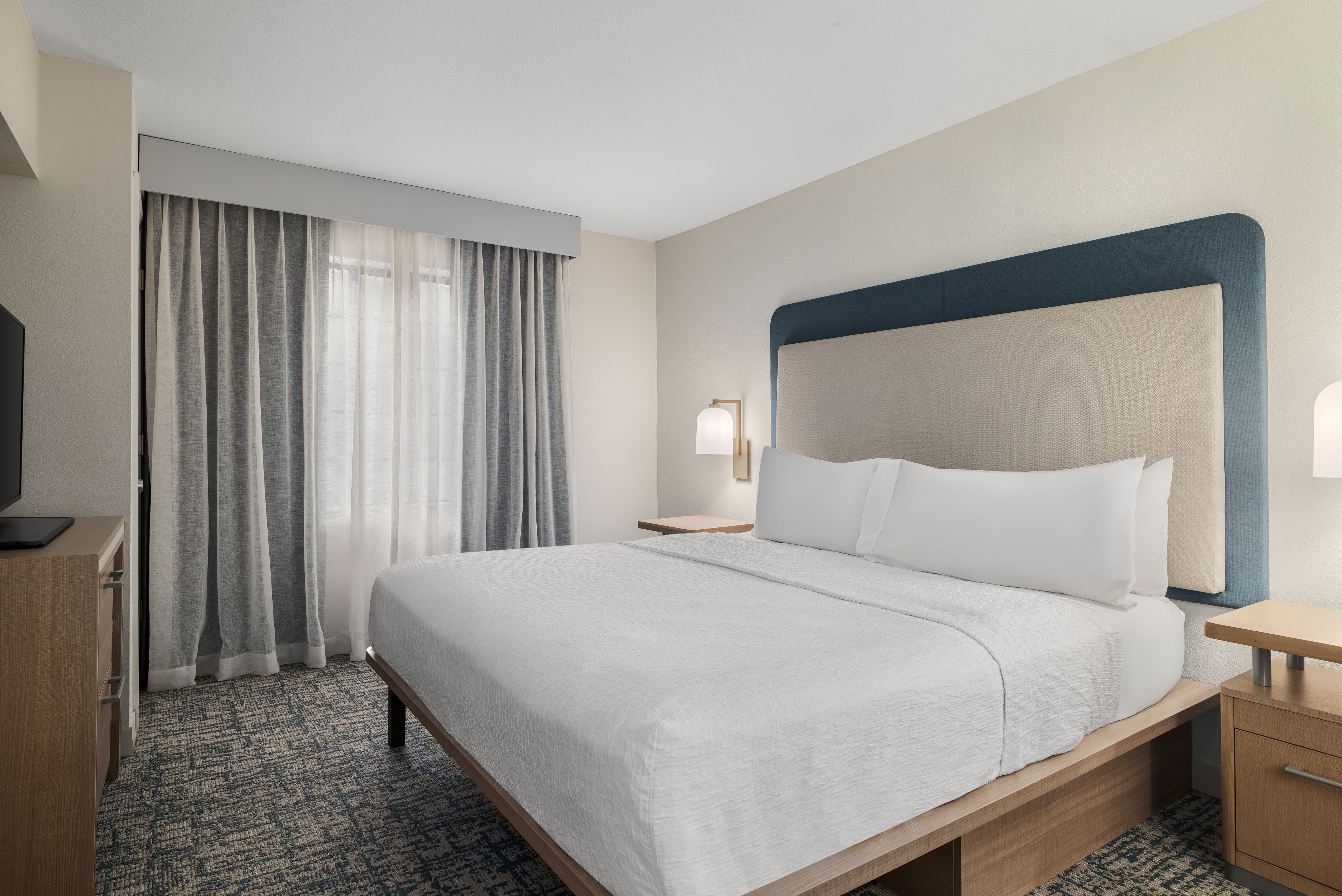 A hotel room with a large bed, a desk, a chair, a television, and a window with curtains.
