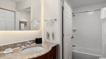 A bathroom with a granite countertop sink, a mirror, a towel rack, and a white bathtub.