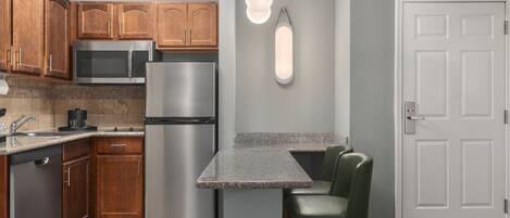 A kitchen with wooden cabinets, stainless steel appliances, a granite countertop, and a green chair.