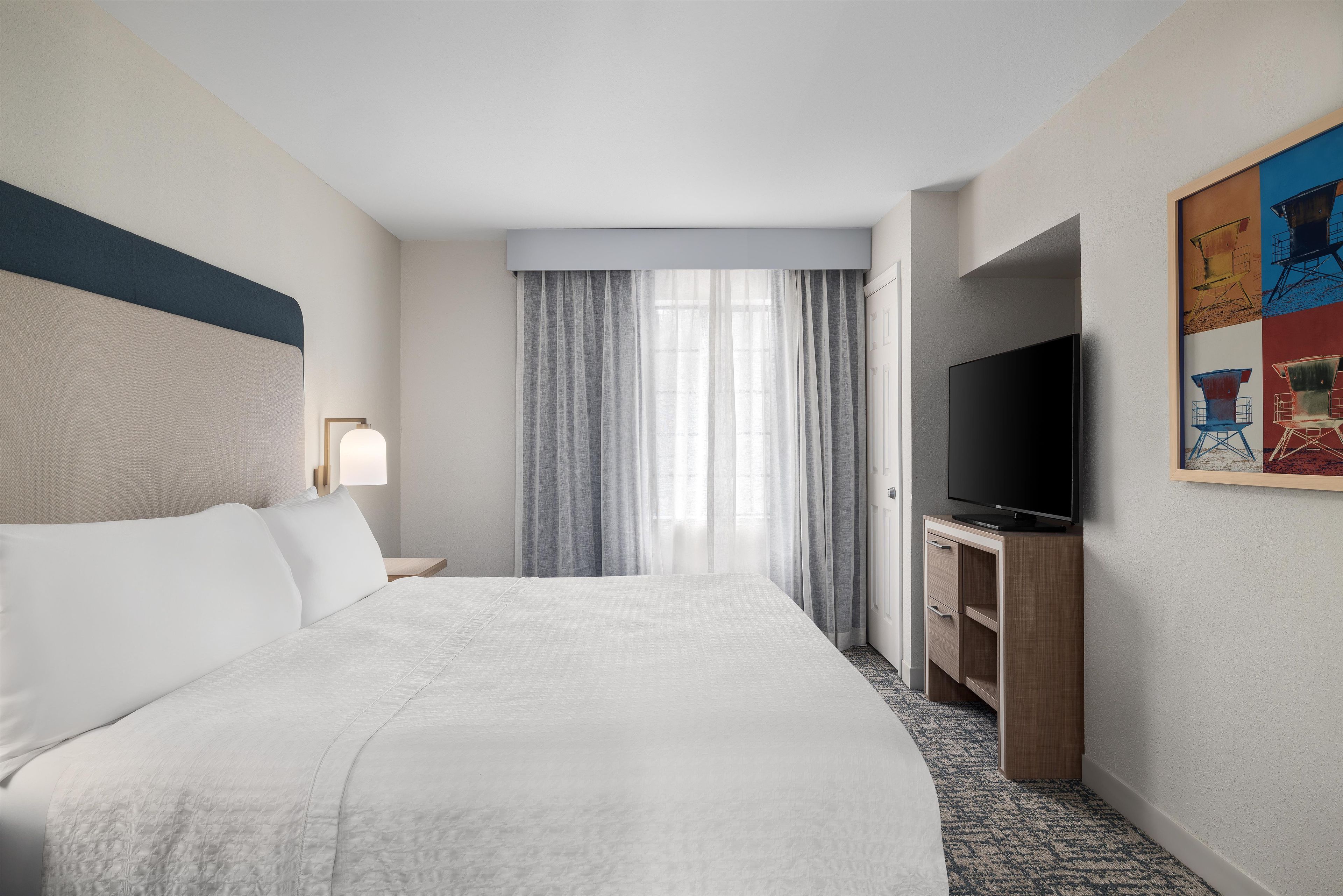 A hotel room with a bed, a television, a desk, and a painting on the wall.