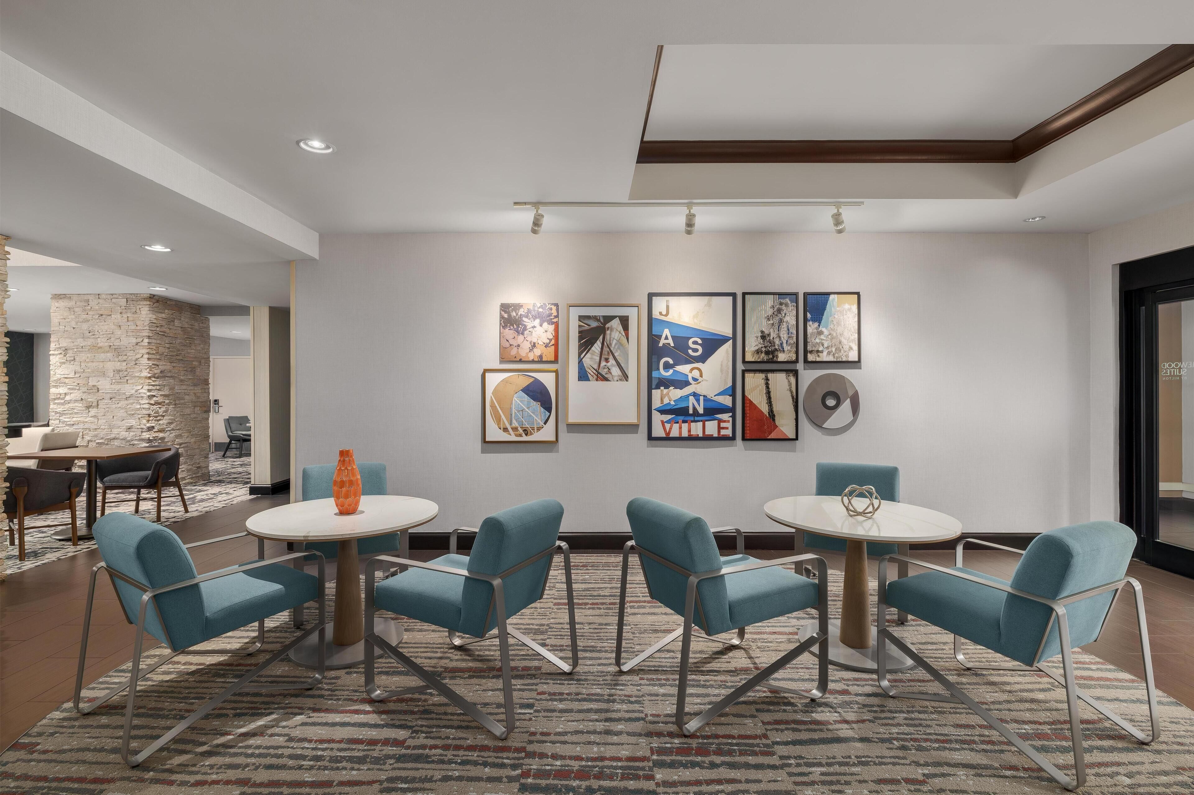 Un hall d’hôtel moderne avec un mur d’accent en pierre, un espace repas avec des chaises bleues et des tables rondes, et des œuvres d’art accrochées aux murs.