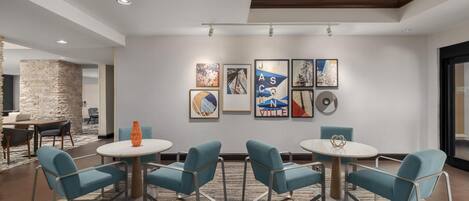 A modern hotel lobby with a stone accent wall, a dining area with blue chairs and round tables, and artwork on the walls.