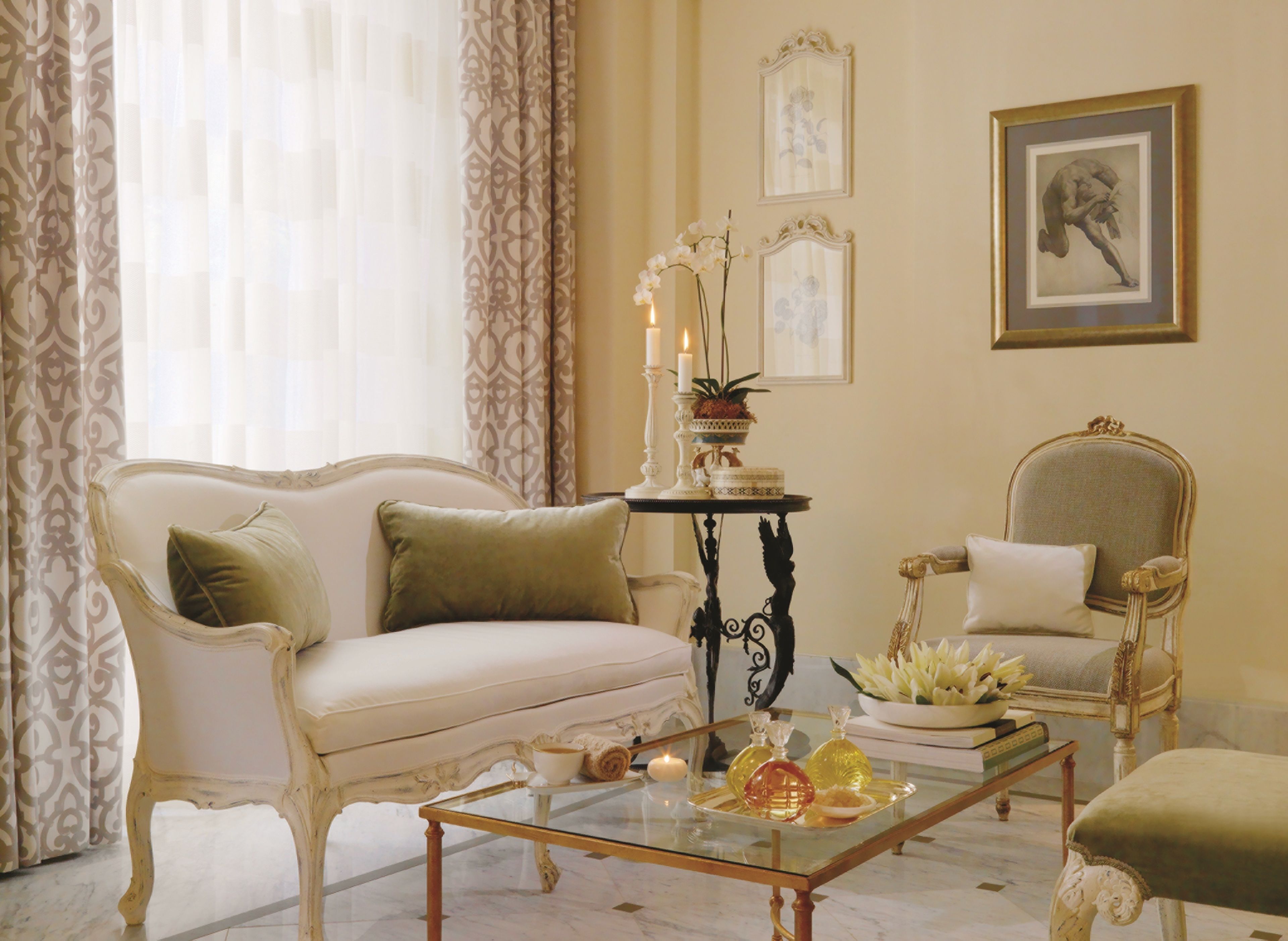 A classic room with a white sofa, a glass coffee table, and a decorative table with candles.