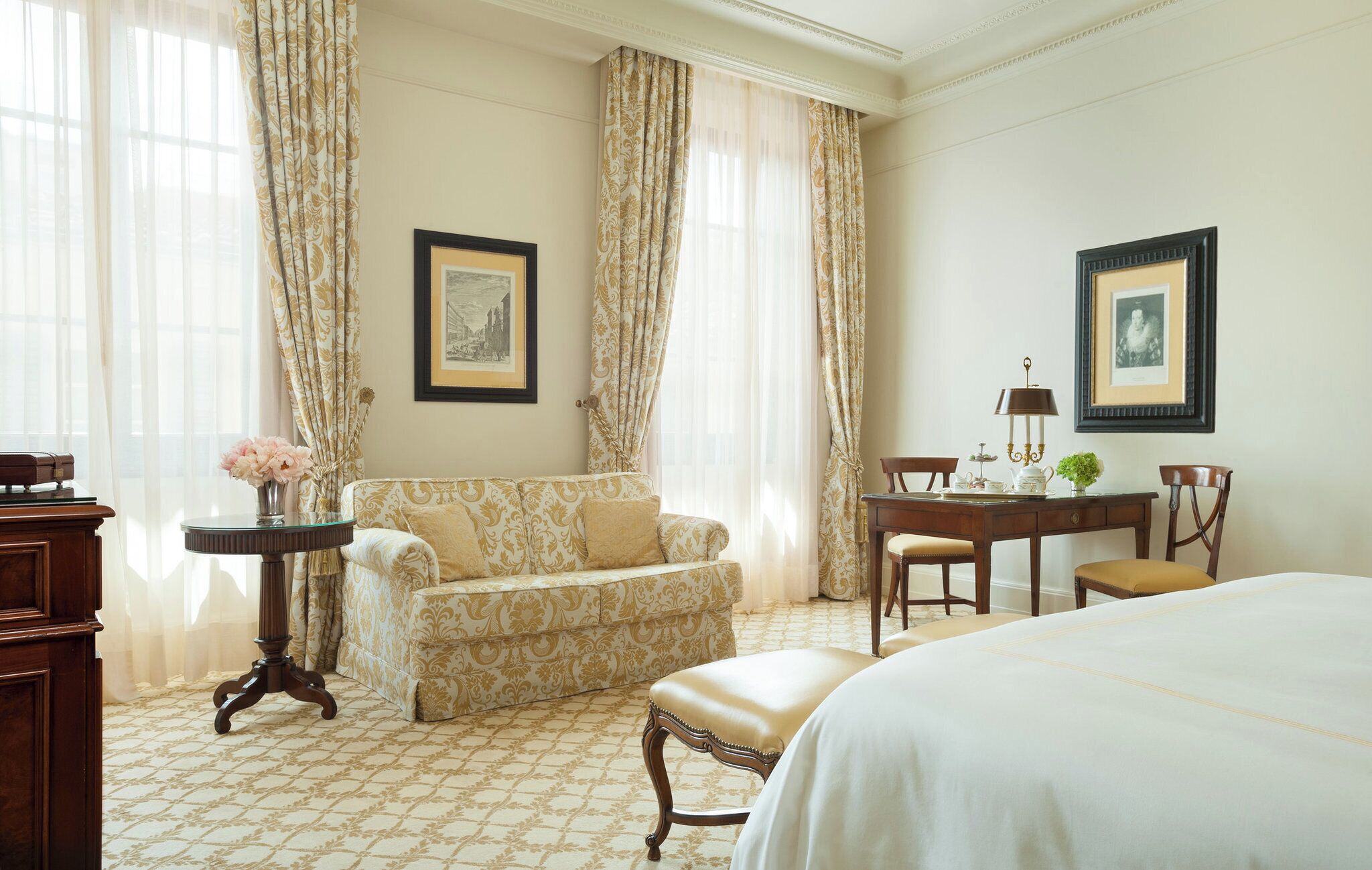 Ein Hotelzimmer mit einer Couch, einem Esstisch mit Stühlen, einem Bett und zwei gerahmten Bildern an den Wänden.