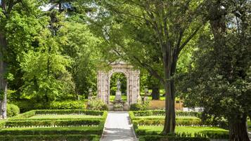 Un giardino formale con un arco centrale, siepi curate e alberi imponenti.