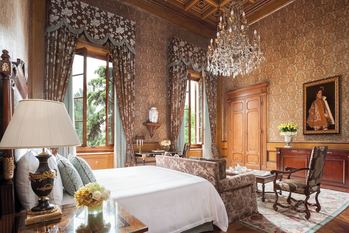 A classic room with a large bed, a wooden desk, a chair, and a chandelier.