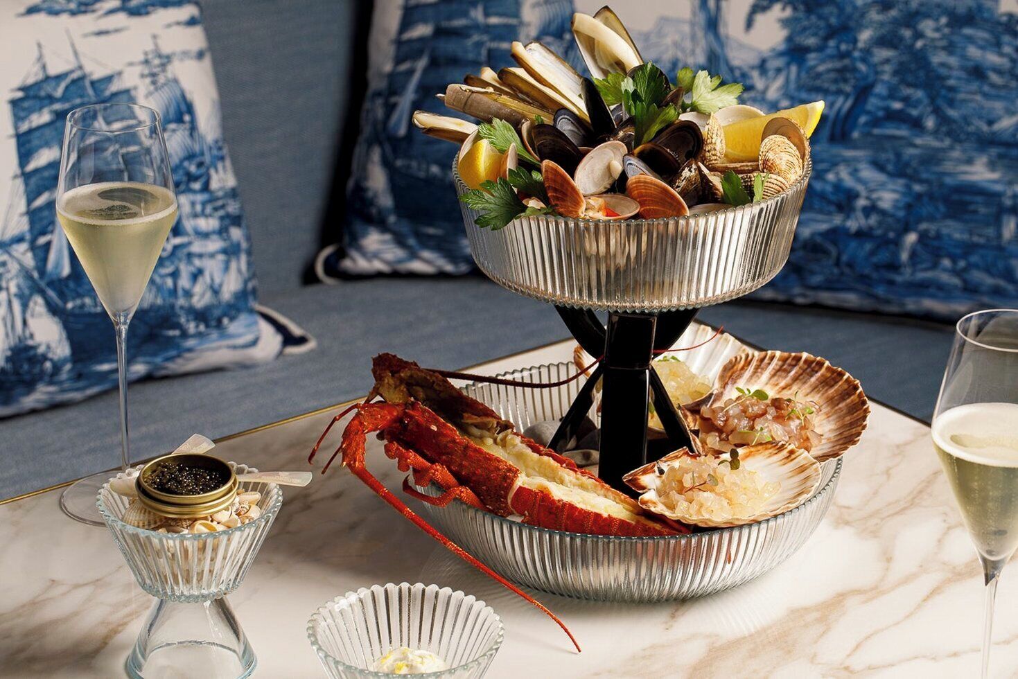 Un plateau de fruits de mer comprenant des palourdes, des moules et un homard, servi sur une table avec un verre de vin blanc et une queue de homard.