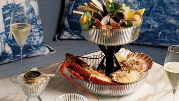 Un plateau de fruits de mer comprenant des palourdes, des moules et un homard, servi sur une table avec un verre de vin blanc et une queue de homard.