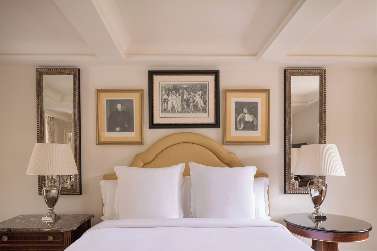 Habitación de hotel con cama, dos mesitas de noche con lámparas, cabecero y tres cuadros en la pared.
