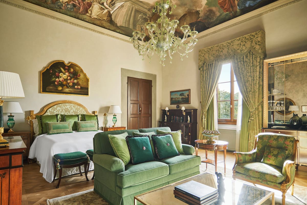 Una habitación amplia con una cama grande, un sofá verde, una mesita y una silla.