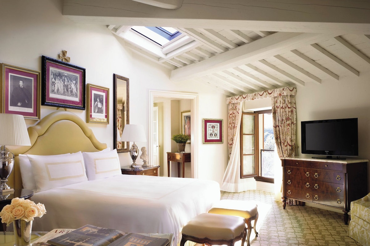 A hotel room with a large bed, a television, a dresser, and framed pictures on the wall.