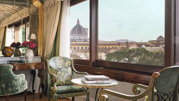 A room with a view of a historic building, a table with books, and two upholstered chairs.