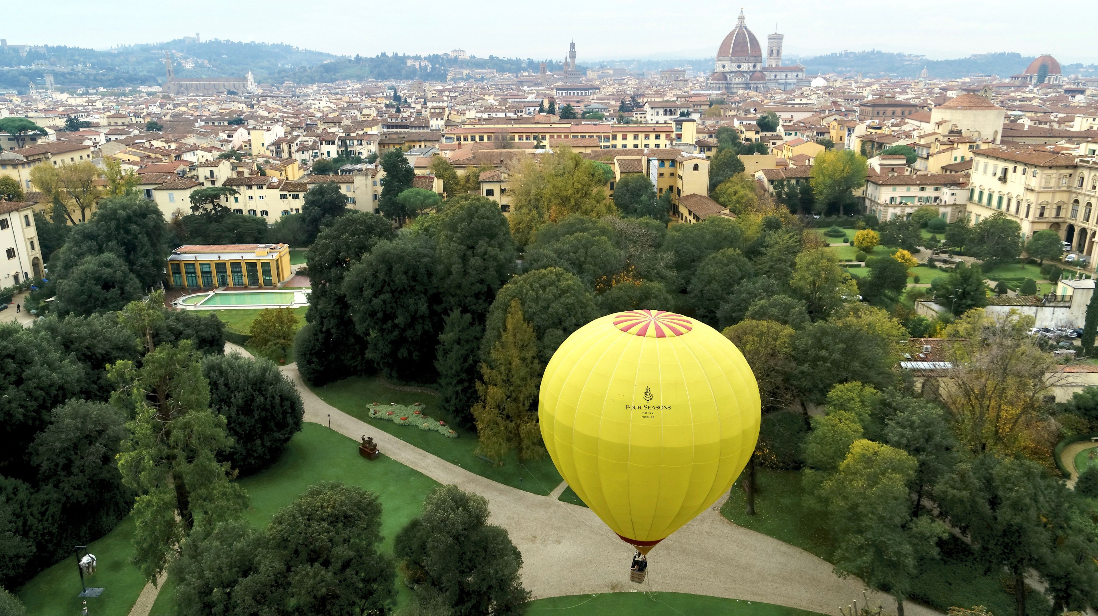 A hot air balloon over a park with a cityscape in the background.