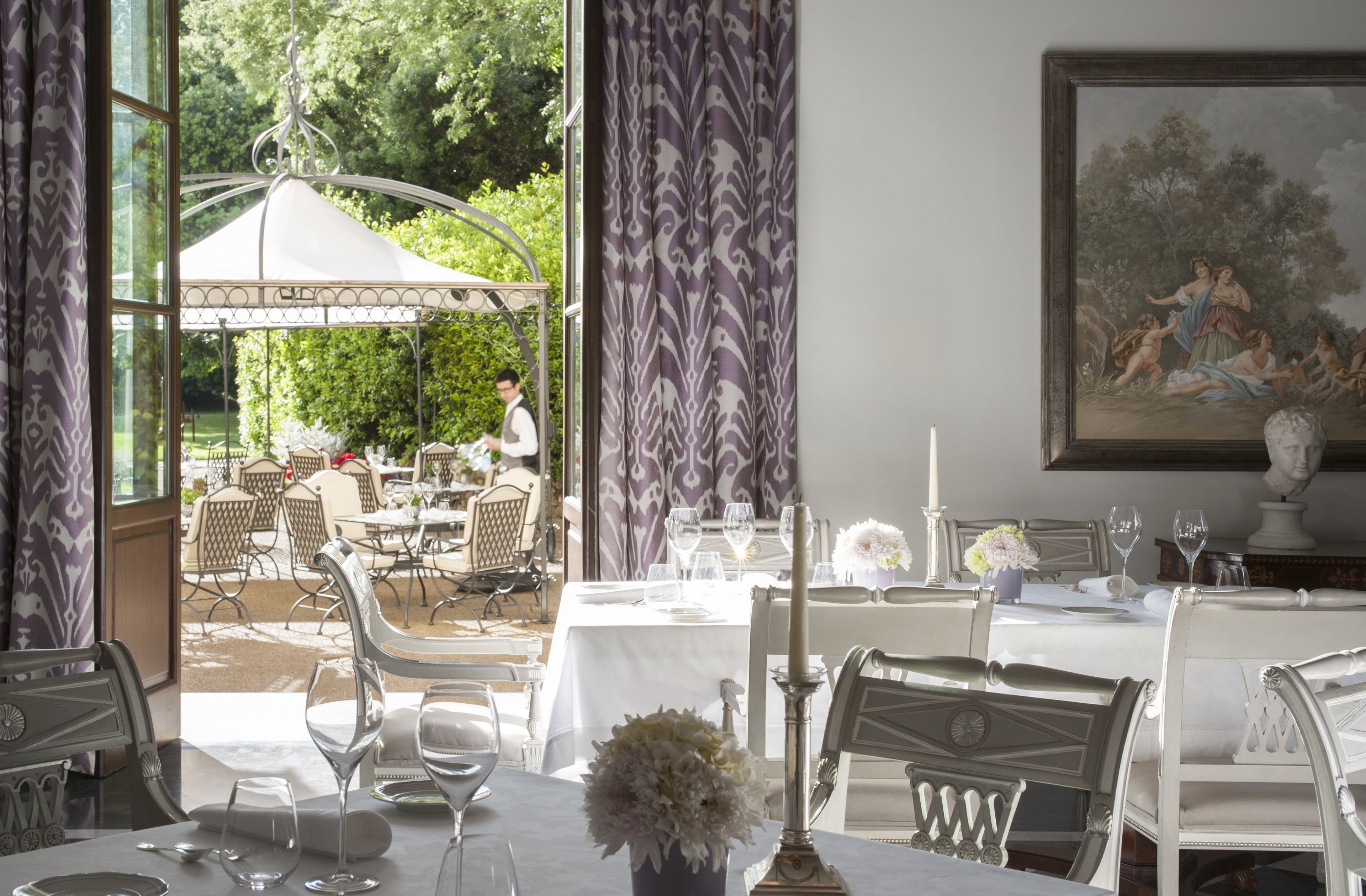 Un comedor con mesas dispuestas para una comida, un cuadro en la pared y vistas al jardín.
