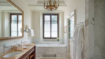 A luxurious bathroom with a double sink, a large mirror, a chandelier, and a bathtub.