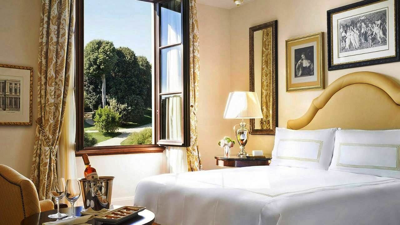 A hotel room with a large bed, a bedside table with a lamp, a window with curtains, and framed pictures on the wall.