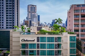 Un hotel con jardín en la azotea, varios pisos y el horizonte de la ciudad al fondo.