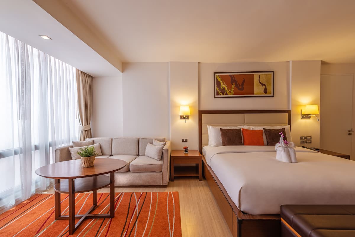 A hotel room with a bed, a sofa, a small table, and a window with curtains.