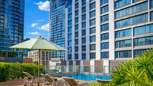 A rooftop pool area with lounge chairs and an umbrella, surrounded by high-rise buildings.